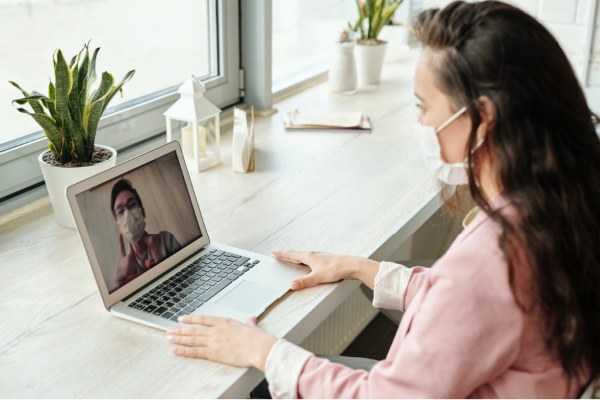 A woman wearing a mask on a laptop engaged on a video call.