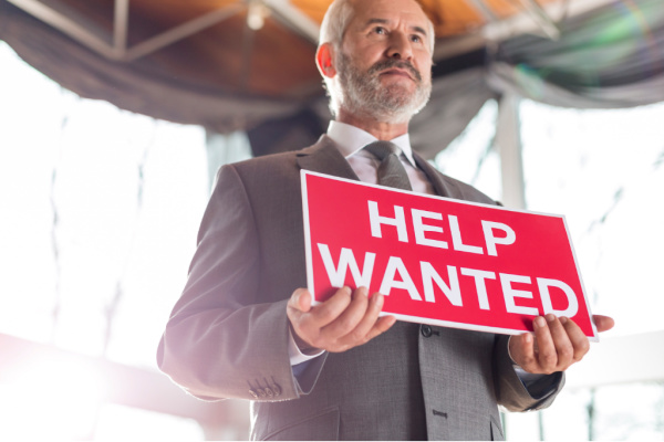 A man in a suit holding a help wanted sign.