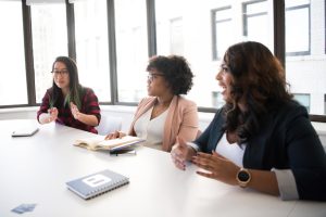 Three women discussing business ideas at a table in a meeting room.