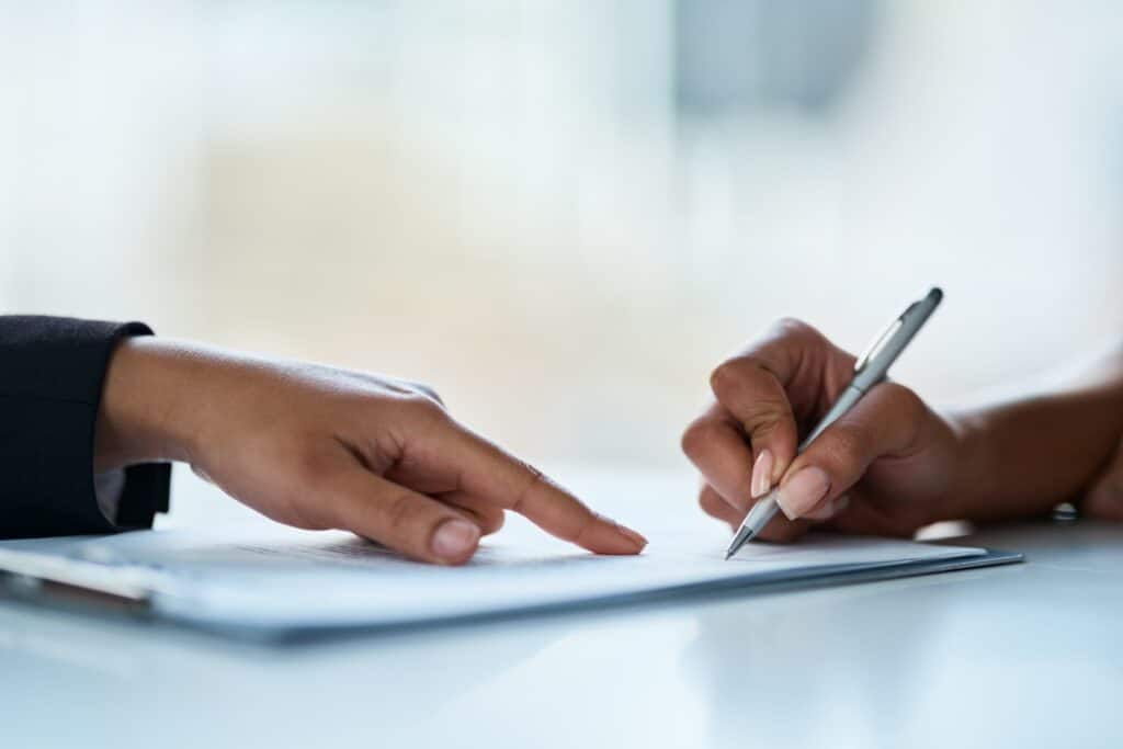 hands on desk, one hand is pointing to another that is holding a pen in it